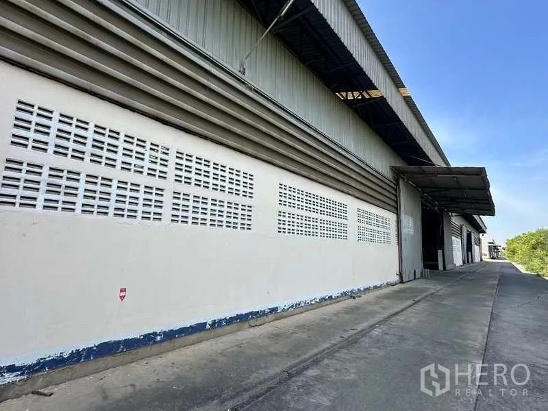 货栈 出租在Wang Noi, Phra Nakhon Si Ayutthaya - 仓库侧立面，通风砖墙与有顶装卸月台，沿混凝土车道分布。