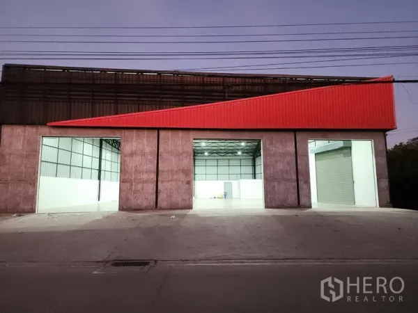 Warehouse for rent in Pak Kret, Nonthaburi - Evening facade of the warehouse highlighting three illuminated loading bays and a red canopy.