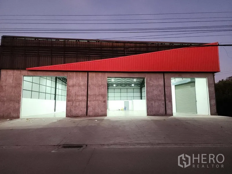 Warehouse for rent in Pak Kret, Nonthaburi - Evening facade of the warehouse highlighting three illuminated loading bays and a red canopy.