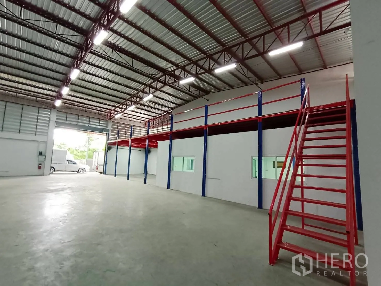 Warehouse for rent in Lat Krabang, Bangkok - Interior view toward the entrance showing mezzanine with windows and a red staircase.