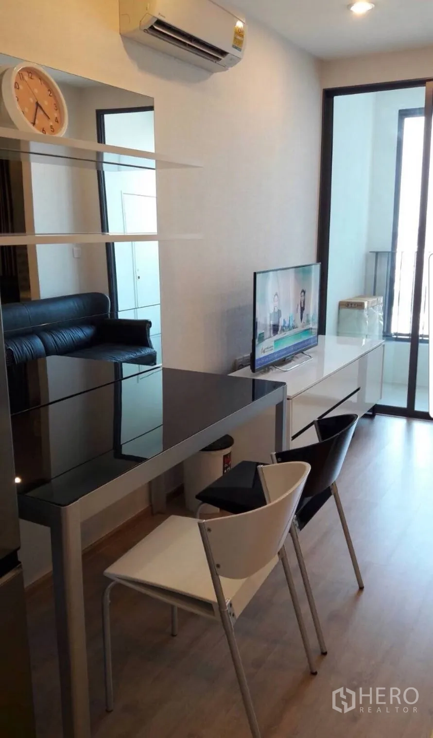 Condominium for rent in Bang Rak, Bangkok - Work-and-dine nook with glass-top table, TV console, air conditioner and balcony access.