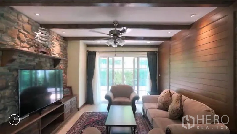 Detached House for rent or sale in Bang Phli, Samut Prakan - Living room with stone accent wall, TV console, ceiling fan and sofa set facing the garden.