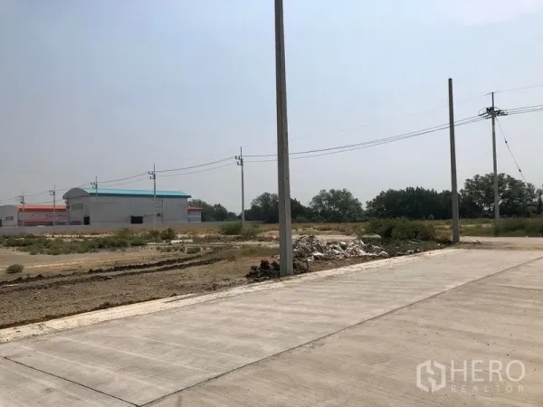 地 出售在Mueang Samut Sakhon, Samut Sakhon - 混凝土路口与电线杆，背景有工厂仓库与开阔荒地