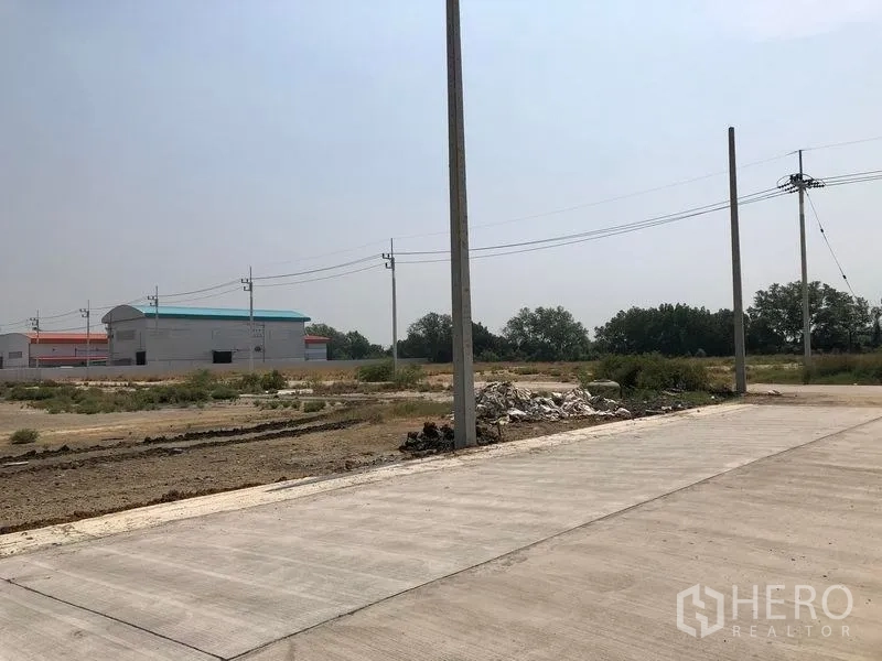 地 出售在Mueang Samut Sakhon, Samut Sakhon - 混凝土路口与电线杆，背景有工厂仓库与开阔荒地