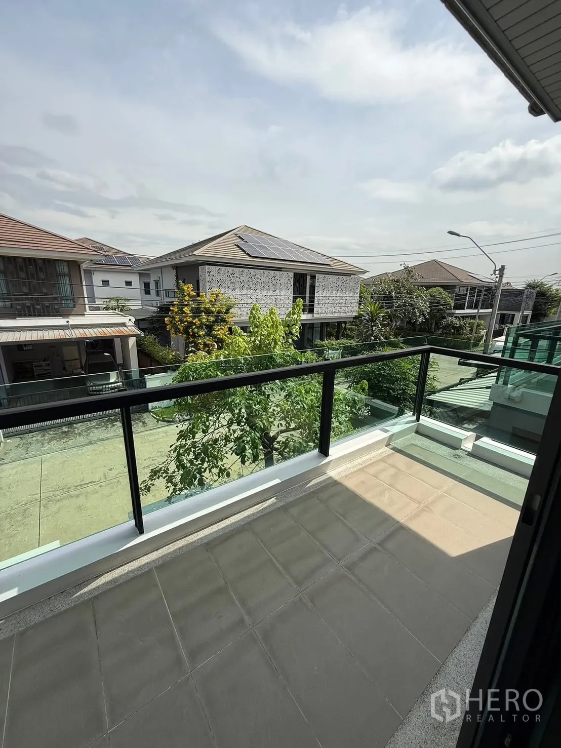 Detached House for rent in Prawet, Bangkok - Upper-floor balcony with glass railing overlooking a quiet residential street and neighboring homes.