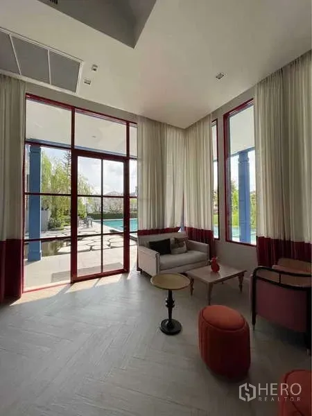 Detached House for rent in Prawet, Bangkok - Sunlit clubhouse lounge with floor‑to‑ceiling windows overlooking the pool and garden.