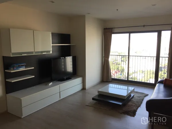 公寓 出租或出售在Khlong Toei, Bangkok - 明亮客厅设媒体墙与茶几，落地推拉门通向阳台，享城市景观。