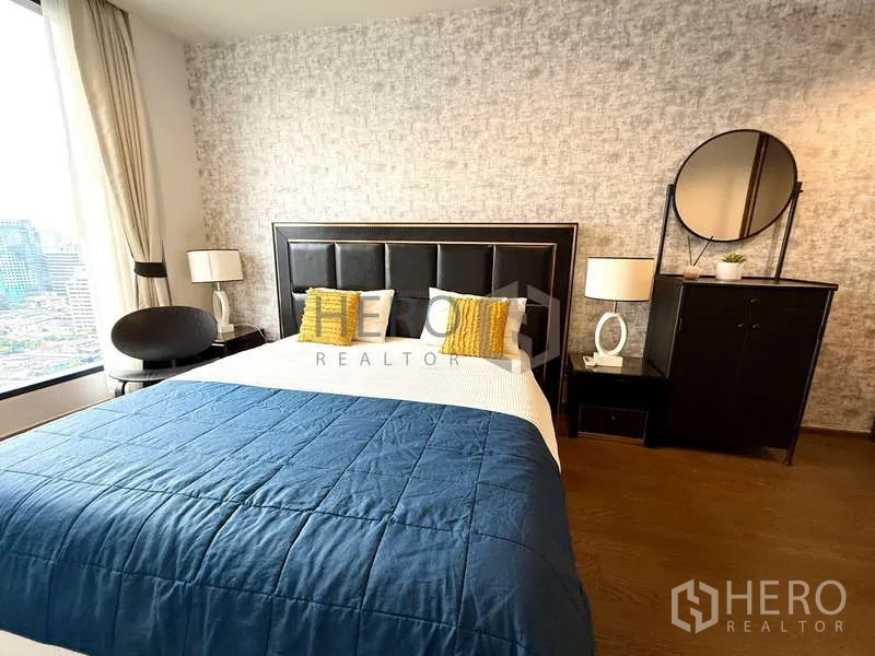 คอนโด ให้เช่า - ห้องนอนสว่าง เตียงหัวเบาะ ผ้าห่มสีน้ำเงิน และหน้าต่างชมวิวเมือง