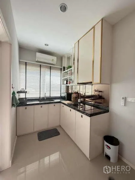 独立式住宅 出售在Bang Khen, Bangkok - L形厨房，白色柜体、黑色台面与百叶窗。