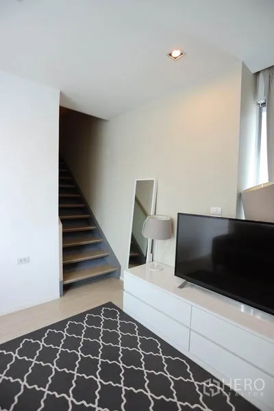 Condominium for rent or sale in Watthana, Bangkok - TV console corner with floor lamp and a staircase adjacent to the living area.