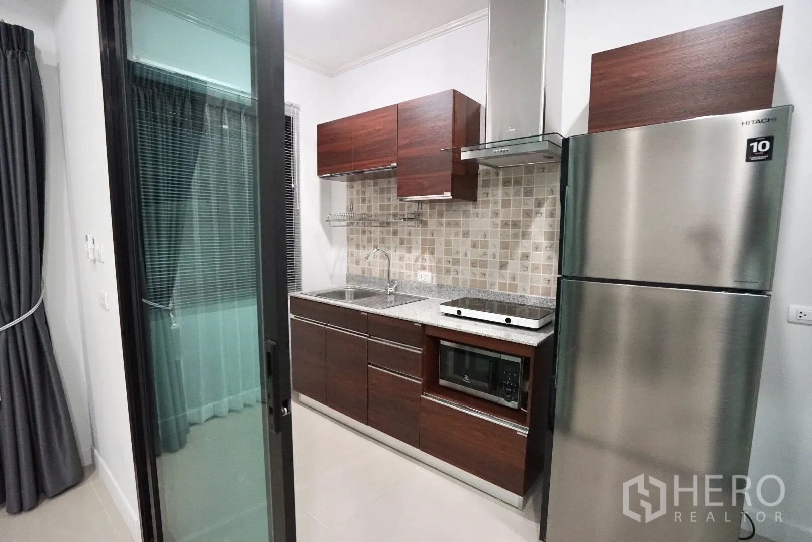 Townhouse for rent in Bang Kapi, Bangkok - Compact built-in kitchen with wooden cabinetry, electric hob, hood, microwave and stainless fridge.