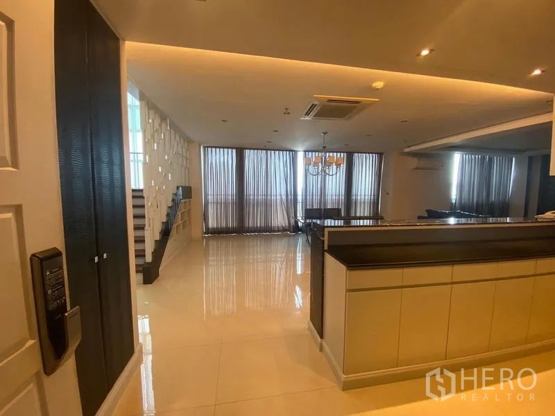 Condominium for rent in Bang Kapi, Bangkok - Entry to a spacious living–dining area with glossy floors, kitchen counter and staircase beside tall curtained windows.