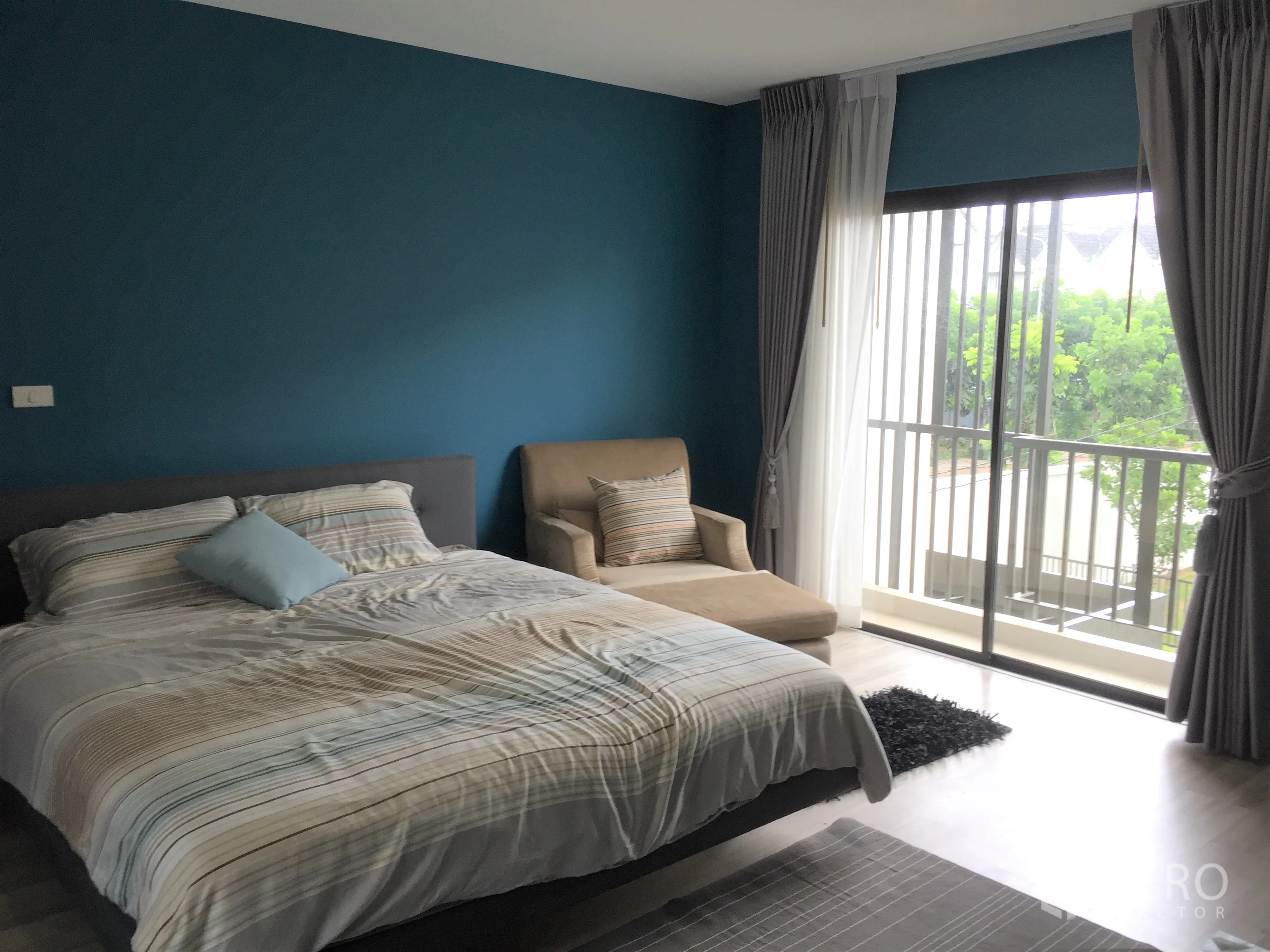 Townhouse for rent in Saphan Sung, Bangkok - Spacious master bedroom with teal accent wall and balcony accessed by floor-to-ceiling sliders.