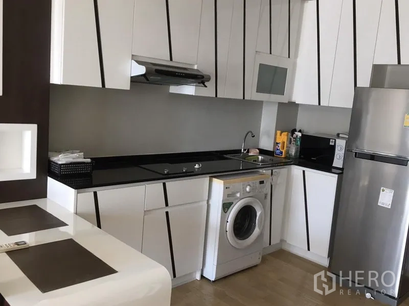 คอนโด ให้เช่าในBangkok - ครัวบิวท์อินสไตล์โมเดิร์น ตู้สีขาว ท็อปสีดำ เตาไฟฟ้า เครื่องซักผ้า และตู้เย็นสแตนเลส