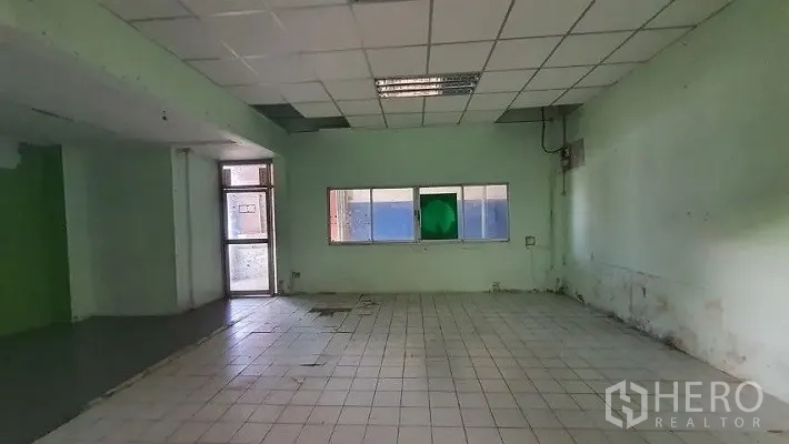 Warehouse for rent in Phra Samut Chedi, Samut Prakan - Tiled office room inside the warehouse with drop ceiling, fluorescent lighting and an exterior window.