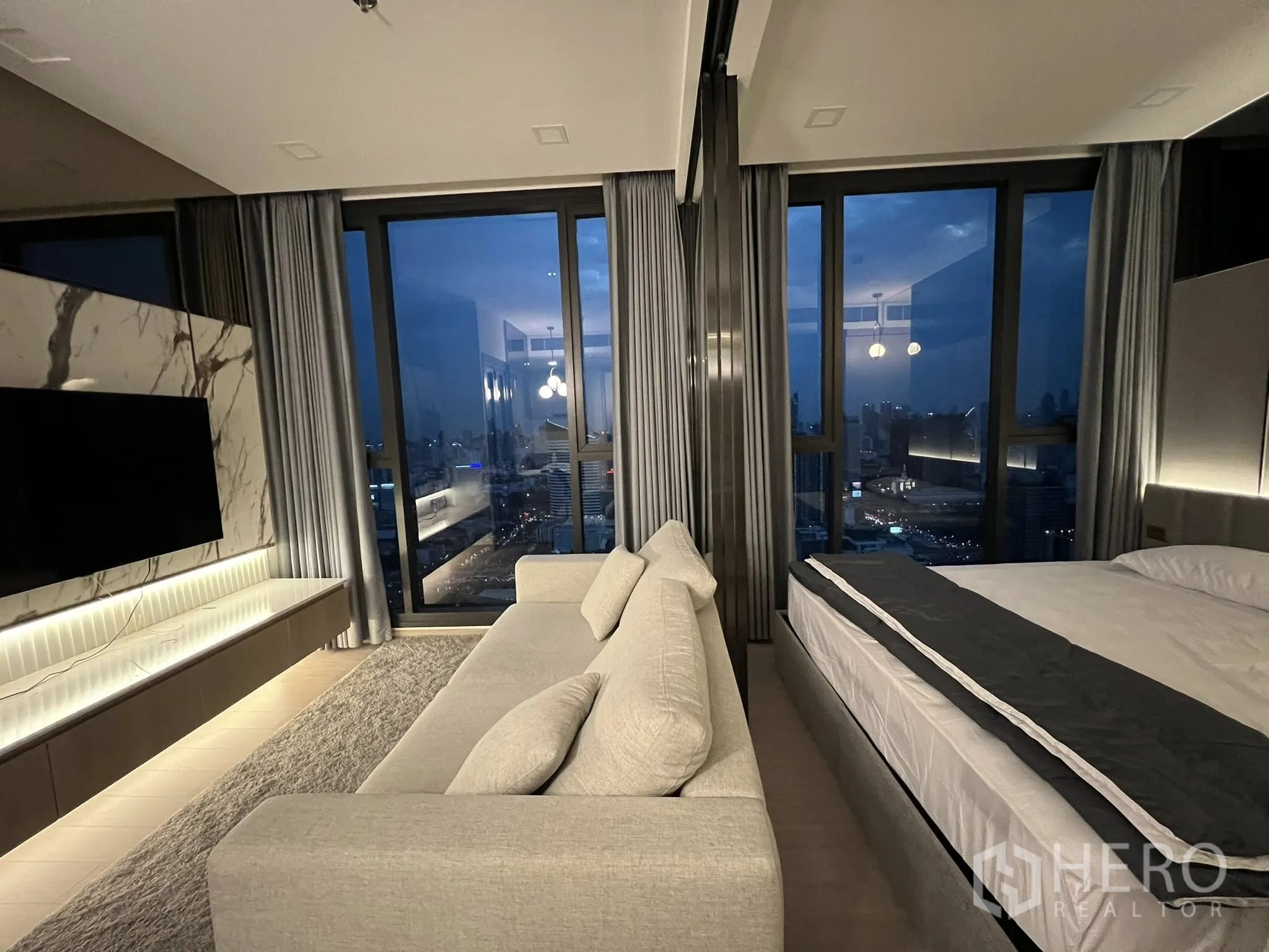 公寓 for rent in Huai Khwang, Bangkok - 高楼层起居区与玻璃隔断卧室，落地窗、大理石电视墙、沙发与夜景。