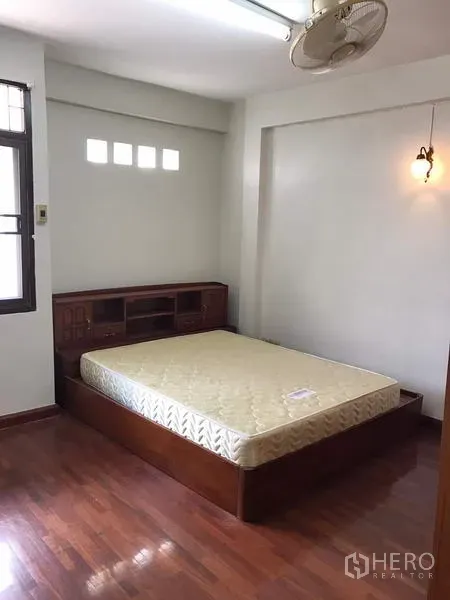 Townhouse for rent in Khlong Toei, Bangkok - Bright bedroom with wooden platform bed, parquet floor and wall fan.
