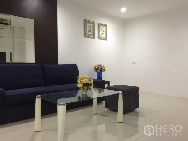 Condominium for rent in Watthana, Bangkok - Bright living room with navy sofa, glass coffee table, ottoman and floral decor.