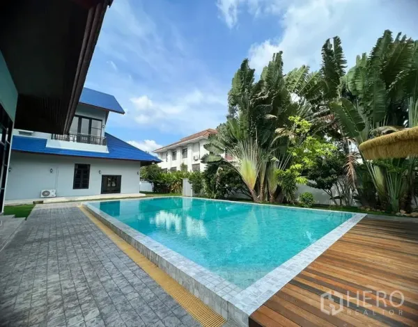 Detached House for sale in Prawet, Bangkok - Large rectangular pool beside a two-storey house with blue roof and patio.