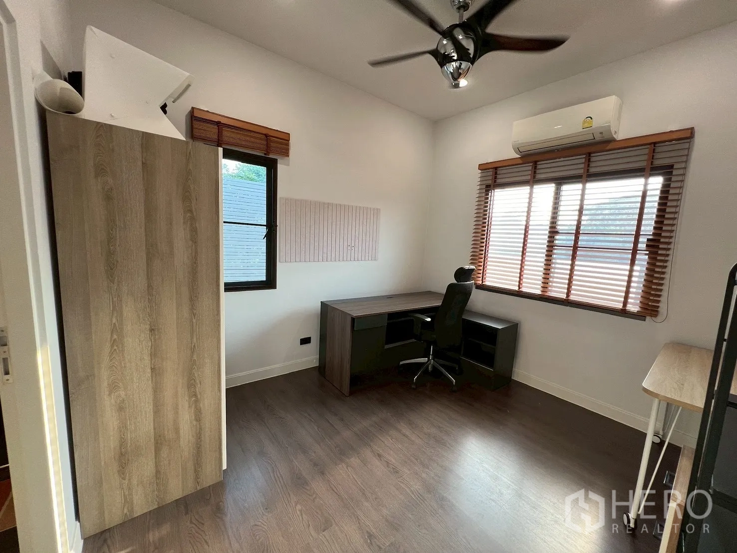 独栋房屋 for rent in Bang Kapi, Bangkok - 明亮的书房，L形书桌、木地板、吊扇与百叶窗。