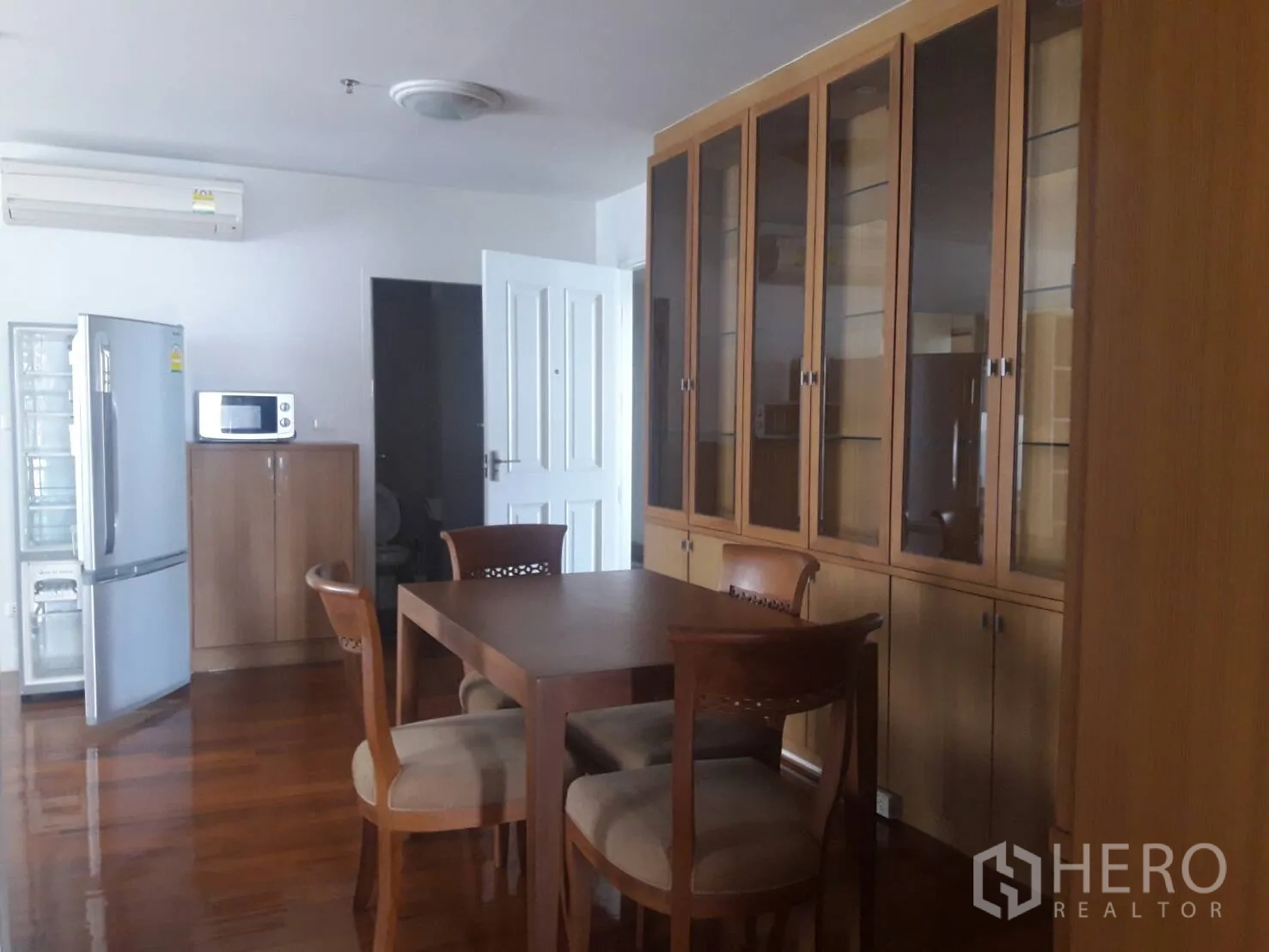คอนโด ให้เช่าในKhlong Toei, Bangkok - มุมรับประทานอาหารพร้อมโต๊ะไม้ เก้าอี้ไม้ ตู้กระจกสูง ตู้ไมโครเวฟและตู้เย็น บนพื้นไม้เงางาม