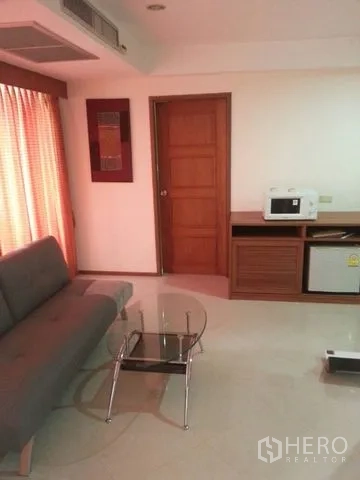 公寓 出租在Bang Rak, Bangkok - 温馨起居角落，配沙发、玻璃桌，以及带微波炉与小冰箱的茶水柜。