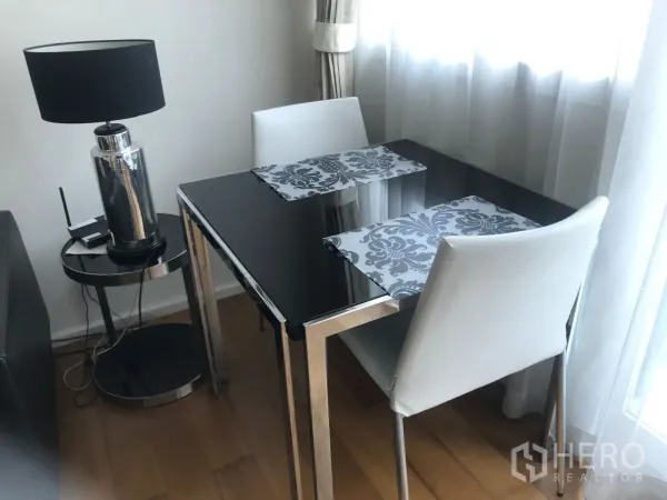 คอนโด ให้เช่าหรือขายในWatthana, Bangkok - มุมรับประทานอาหาร โต๊ะกระจกสีดำ เก้าอี้สีขาวสองตัว และโคมไฟข้างหน้าต่าง