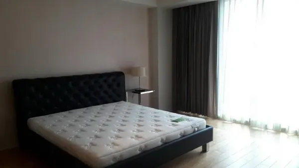 Condominium for sale in Sathon, Bangkok - Sunlit master bedroom with king bed, wood flooring and floor-to-ceiling curtains.