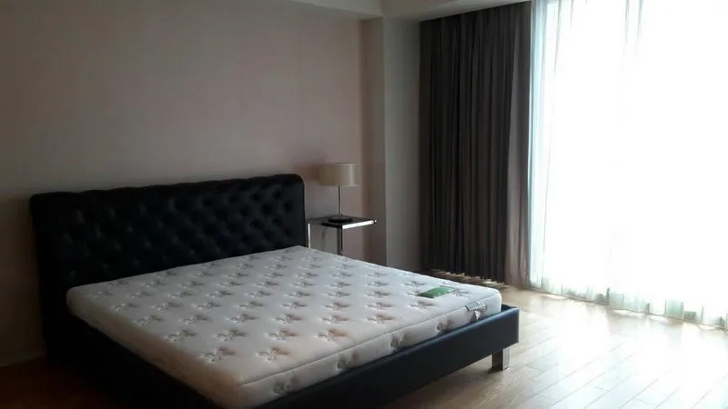 Condominium for sale in Sathon, Bangkok - Sunlit master bedroom with king bed, wood flooring and floor-to-ceiling curtains.