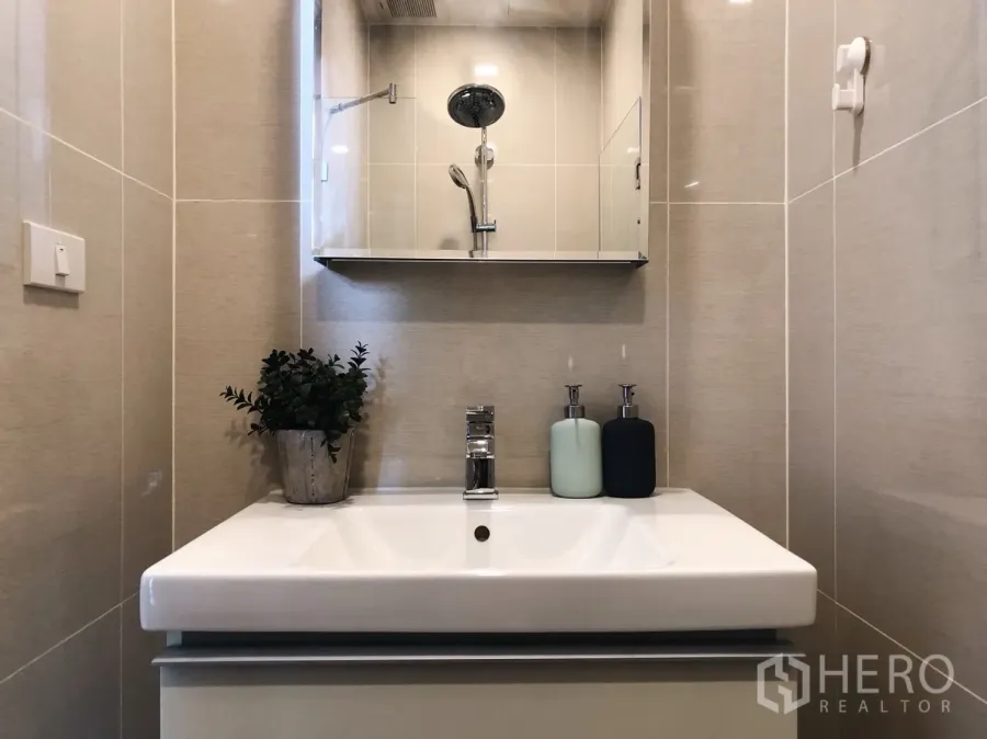 Condominium for rent in Khlong Toei, Bangkok - Modern bathroom with mirror cabinet, rain shower, and white vanity with soap dispensers.