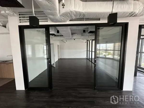 Office Space for rent - Open-plan office with dark wood floors, glass partition doors, and exposed duct ceiling.