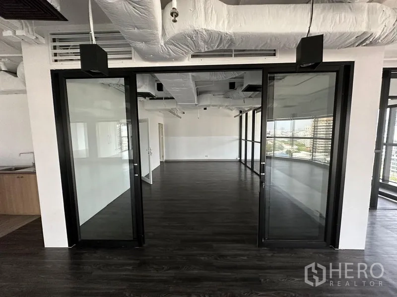 Office Space for rent - Open-plan office with dark wood floors, glass partition doors, and exposed duct ceiling.