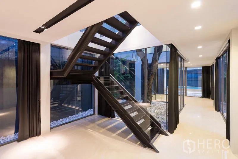 Home Office for rent in Khlong Toei, Bangkok - Open-plan hall with glass walls and a black staircase overlooking the courtyard at dusk.