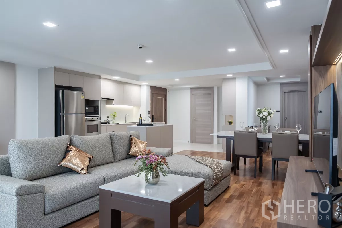 Apartment for rent - Open-plan living room with grey sectional sofa, TV wall and modern kitchen.