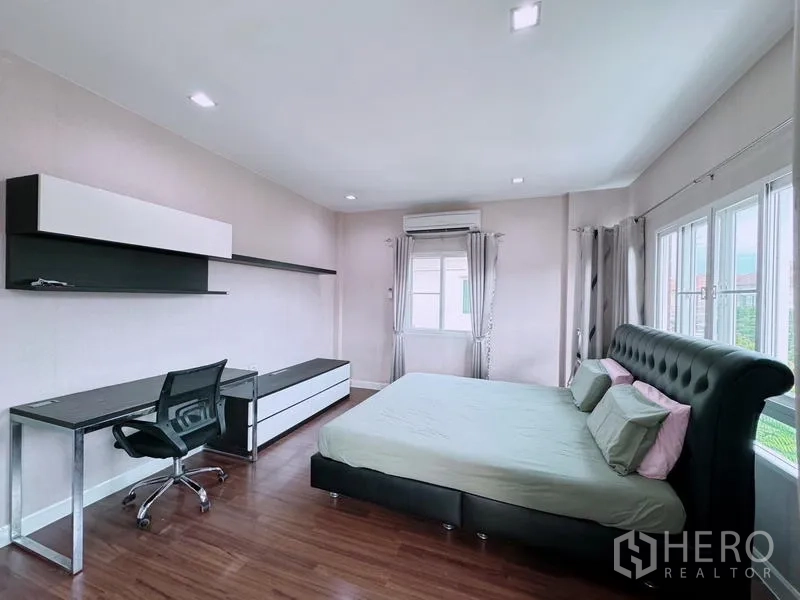 Detached House for rent in Prawet, Bangkok - Master bedroom angle showing built-in desk, shelving, large bed, and AC.