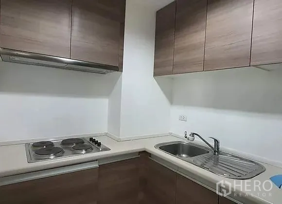Condominium for rent in Huai Khwang, Bangkok - Compact L-shaped kitchen with electric cooktop, hood, sink and upper cabinets.