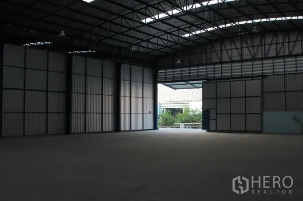 货栈 出租在Lat Krabang, Bangkok - 从仓库内部望向开启的门，可见外部车道与绿化景观。