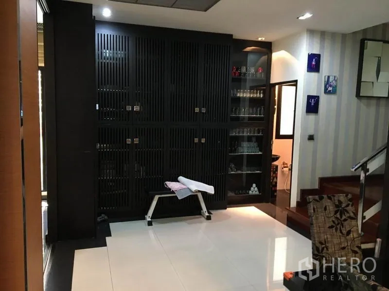 Detached House for rent in Khlong Toei, Bangkok - Hallway with built-in dark wood cabinets, glass display shelves and staircase.