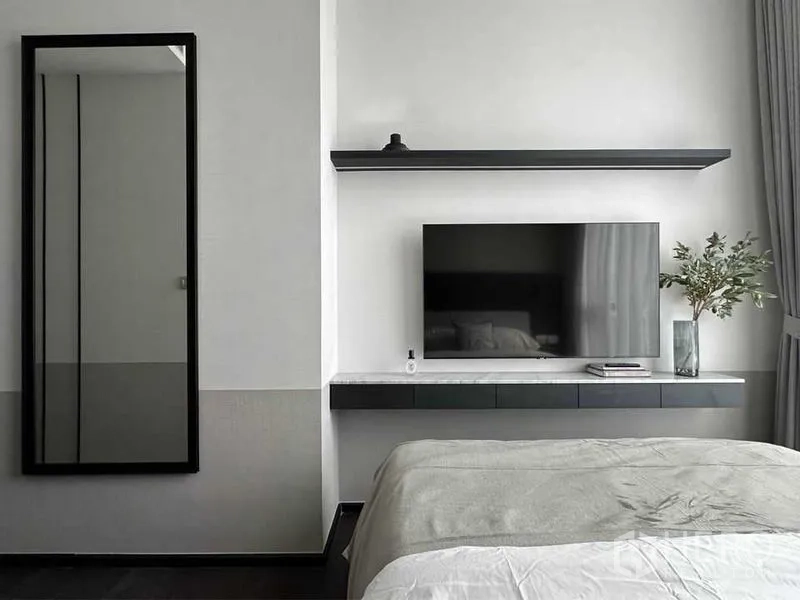 Condominium for rent or sale in Watthana, Bangkok - Minimalist bedroom with wall-mounted TV, floating shelf, full-length mirror and grey bedding.
