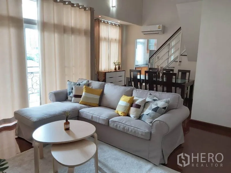 公寓 出租在Watthana, Bangkok - 开放式客餐厅，落地高窗、L形沙发与楼梯景观。