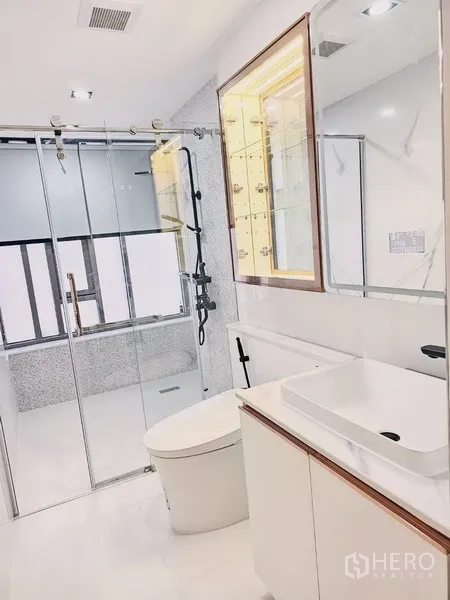 Condominium for sale in Bang Rak, Bangkok - Second bathroom with sliding glass shower, illuminated mirror cabinet and clean white finishes.