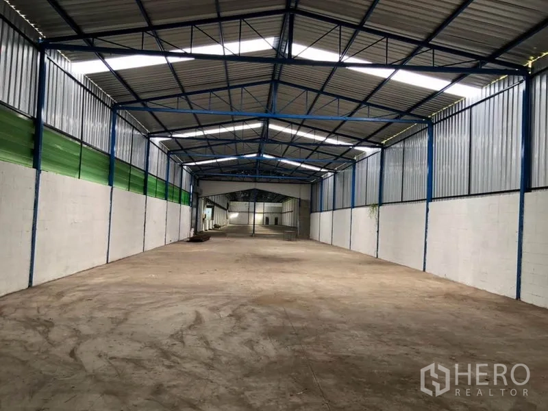 工厂 出租在Nonthaburi - 次仓库区域，钢架屋顶，绿色通风板与开阔的混凝土地面。