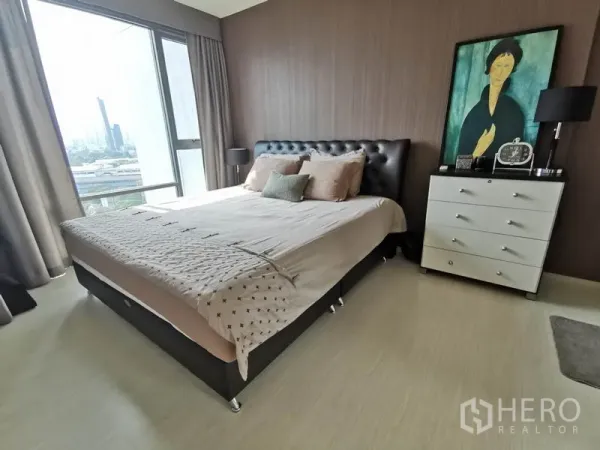 Condominium for rent in Khlong Toei, Bangkok - Bright bedroom with large window, upholstered bed, side lamps and dresser overlooking the city.