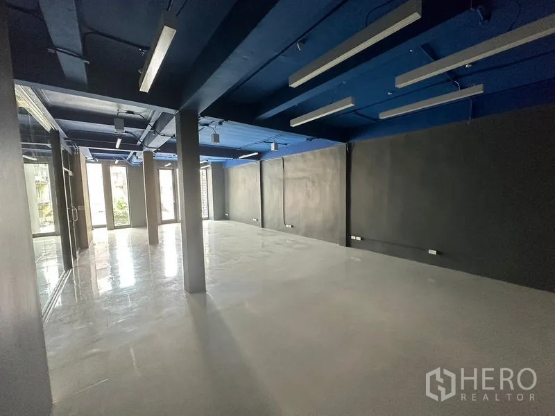 办公空间 出租在Watthana, Bangkok - 开放式办公室，蓝色外露天花、线性LED灯、抛光地面与落地窗。