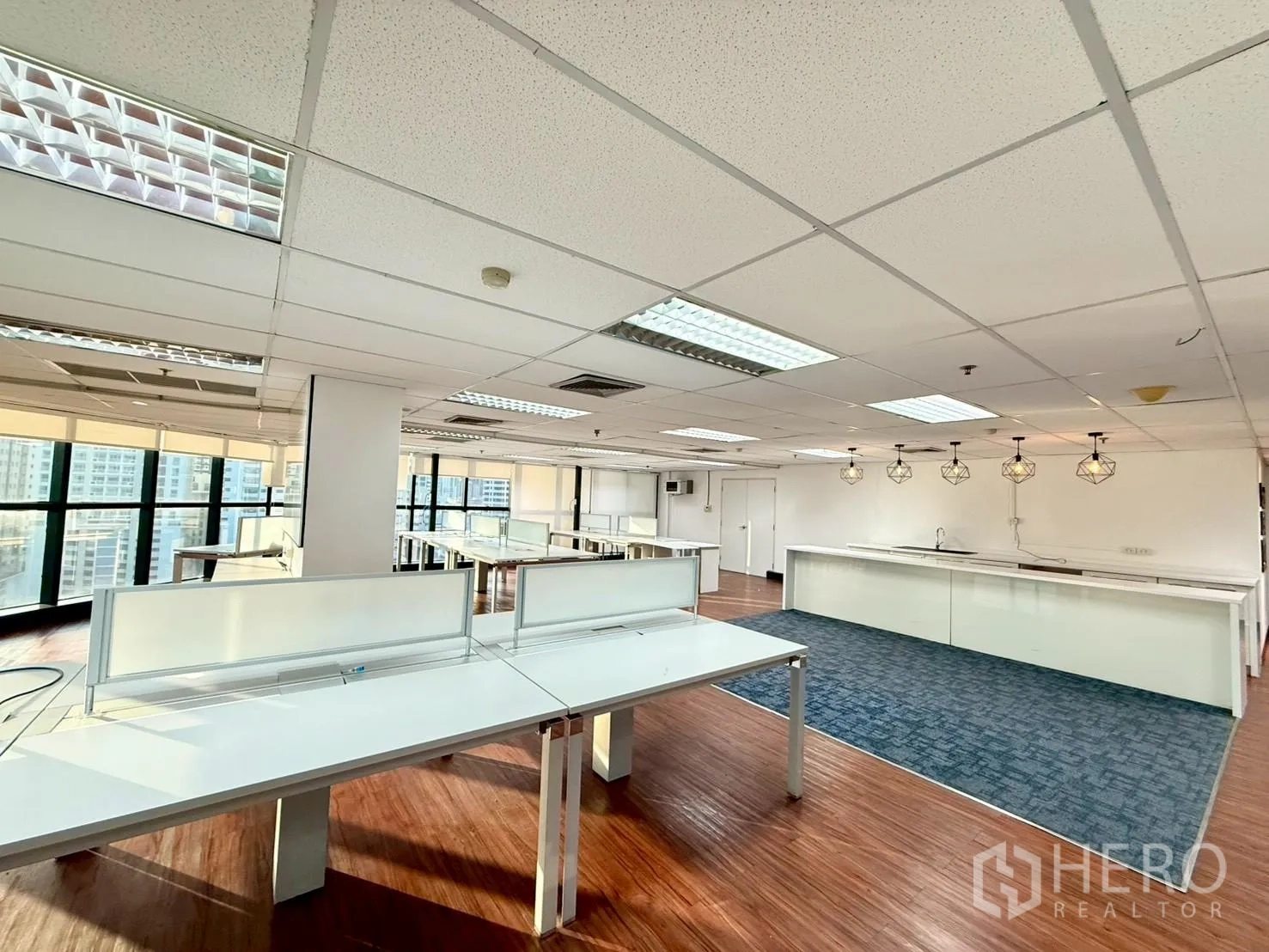 ออฟฟิศ for rent in Watthana, Bangkok - โต๊ะทำงานใกล้มุมกระจกมองเห็นวิวเมือง พร้อมแพนทรีและโคมไฟแขวนด้านข้าง.