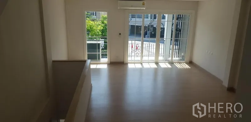 联排别墅 出租在Bang Na, Bangkok - 采光充足的楼层空间，浅色木地板，推拉玻璃门通向阳台。