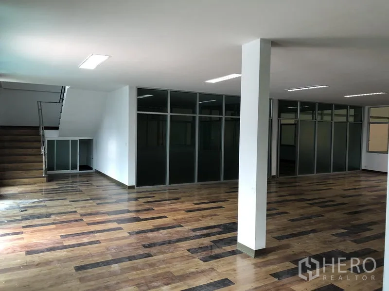 Factory for rent in Samut Prakan - Open‑plan office interior with wood‑look floors, glass partitions and a stair to the upper level.