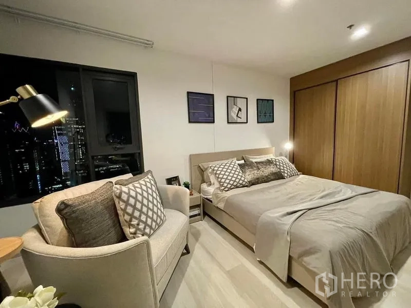 Condominium for rent in Pathum Wan, Bangkok - Bedroom with city-facing window, upholstered bed and large wood wardrobe.