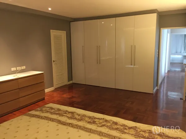 Condominium for rent in Sathon, Bangkok - Spacious master bedroom with glossy wardrobes, dresser, recessed lighting and warm wood floors.