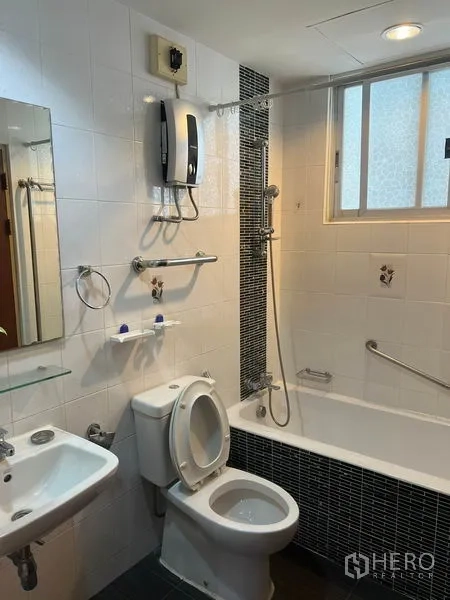 Condominium for rent in Watthana, Bangkok - Tiled bathroom featuring bathtub with shower, toilet, sink and wall-mounted water heater by the window.